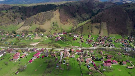 Revelación-Aérea-De-Un-Pintoresco-Pueblo-De-Montaña-Con-Una-Gran-Cadena-Montañosa-En-El-Fondo,-Montañas-Bucegi,-Rumania