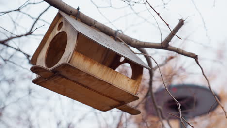 natural wooden birdhouse with round holes suspended securely from tree branch using wire, surrounded by bare autumn twigs and subtle background blur, evoking peaceful seasonal atmosphere