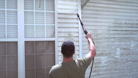 homeowner pressure washes vinyl siding on hot day