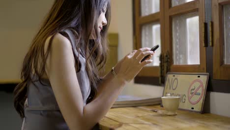 las mujeres asiáticas beben té caliente y juegan al teléfono en el café.