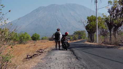 Una-Mujer-Está-Tomando-Su-Casco-De-La-Motocicleta-Para-Comenzar-A-Conducir-En-La-Calle,-Fondo-De-Volcán-En-Indonesia,-Espacio-Para-Copiar,-Estática