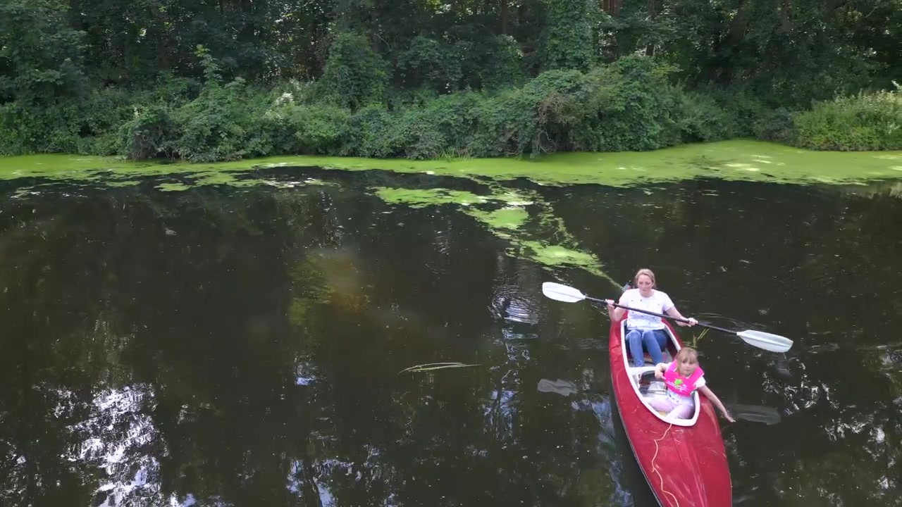 Mooie luchtopname van bovenaf: gezinsvakantie met alleenstaande moeder en kind in een rode peddelboot op een natuurlijke rivier, zomer 2023 Duitsland. Drone beweegt naar rechts, 4K cinematisch.