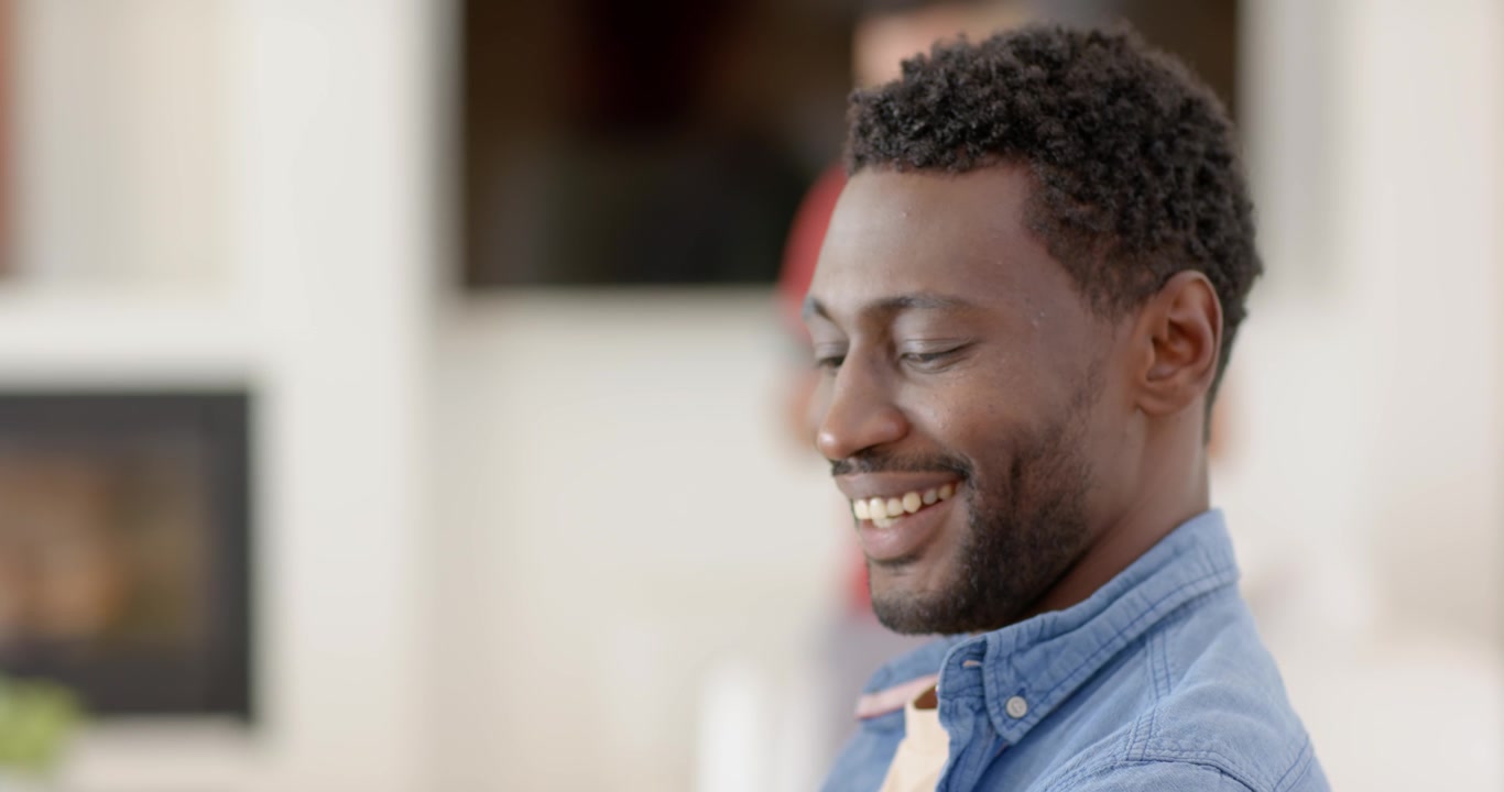 African American man 20s tapping phone at counter after alert, mug headphones smartwatch smiling