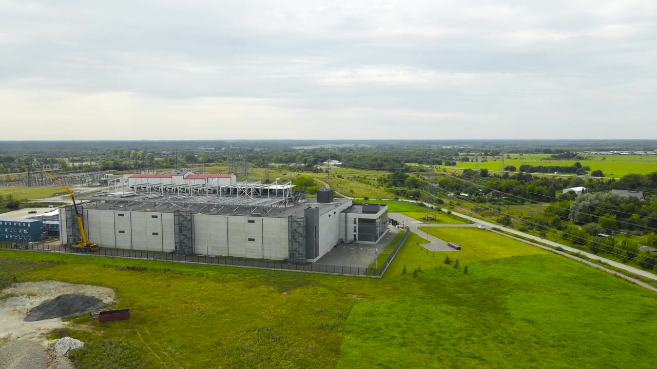 Amplia vista aérea que muestra una instalación de centro de datos a gran escala durante su fase de construcción, con estructura visible, ampliaciones de edificios y el paisaje verde circundante.