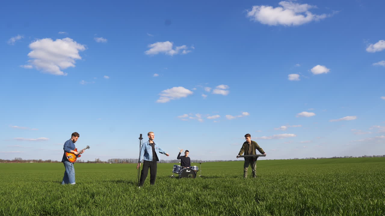 Boys band playing musical instruments and singing song. Music group of four young men performing music in the field in summer.