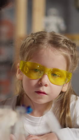 asian man teacher and wondered little girl in protective glasses look at blue litmus test sitting at table during fun science lesson in classroom closeup