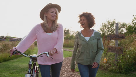 two mature female friends walking along path with bike through yurt campsite