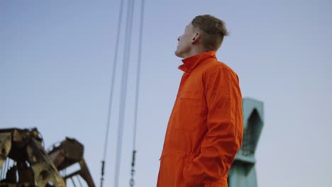 handsome young container warehouse worker in orange uniform standing by the ship at the harbor and looking up