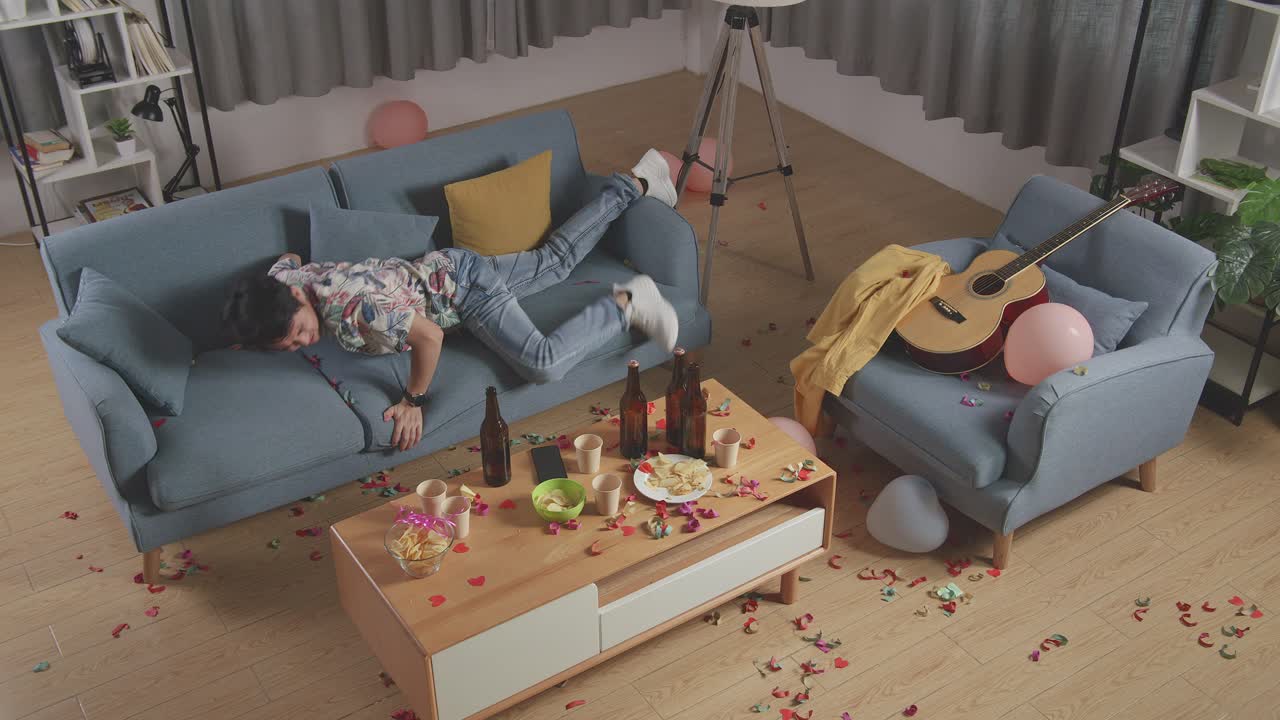 верхний вид пьяного азиатского мужчины просыпается после сна на диване и держит голову руками из-за головной боли в комнате вечеринки дома