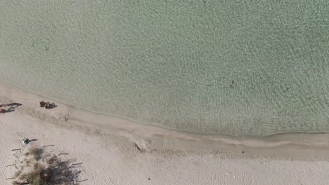 people sitting on mediterranean sea coastline and enjoying sunny day, aerial top down view