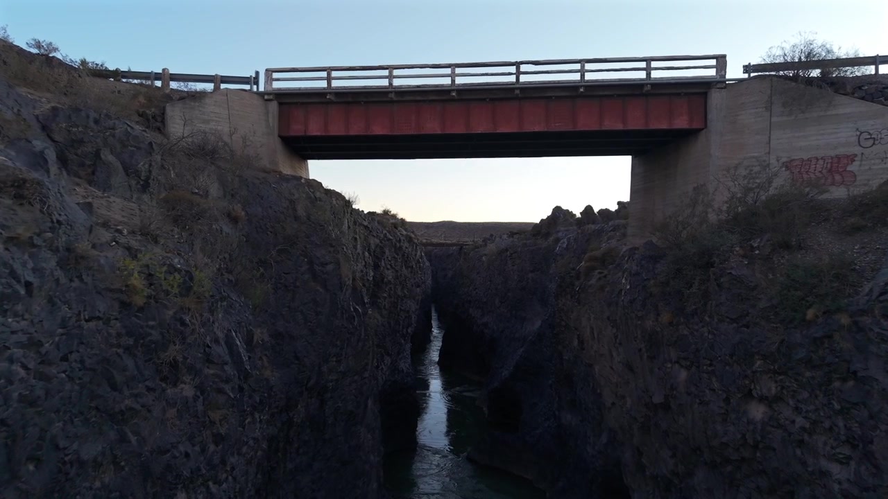 Volcanic canyon carved by the Río Grande in La Payunia near RN40 and Payún Matrú volcanic region, Mendoza, Argentina, featuring basalt rock walls and bridge infrastructure, FPV forward flythrough shot