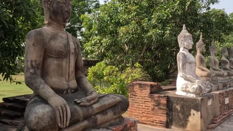 a series of weathered buddha statues sit serenely on brick platforms surrounded by vibrant trees.