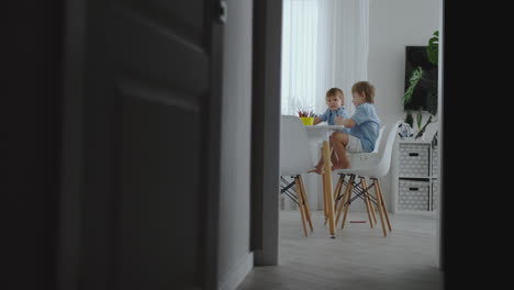 happy family young beautiful mother and two sons draw with colored pencils sitting at the table in the kitchen. the camera moves in slow motion