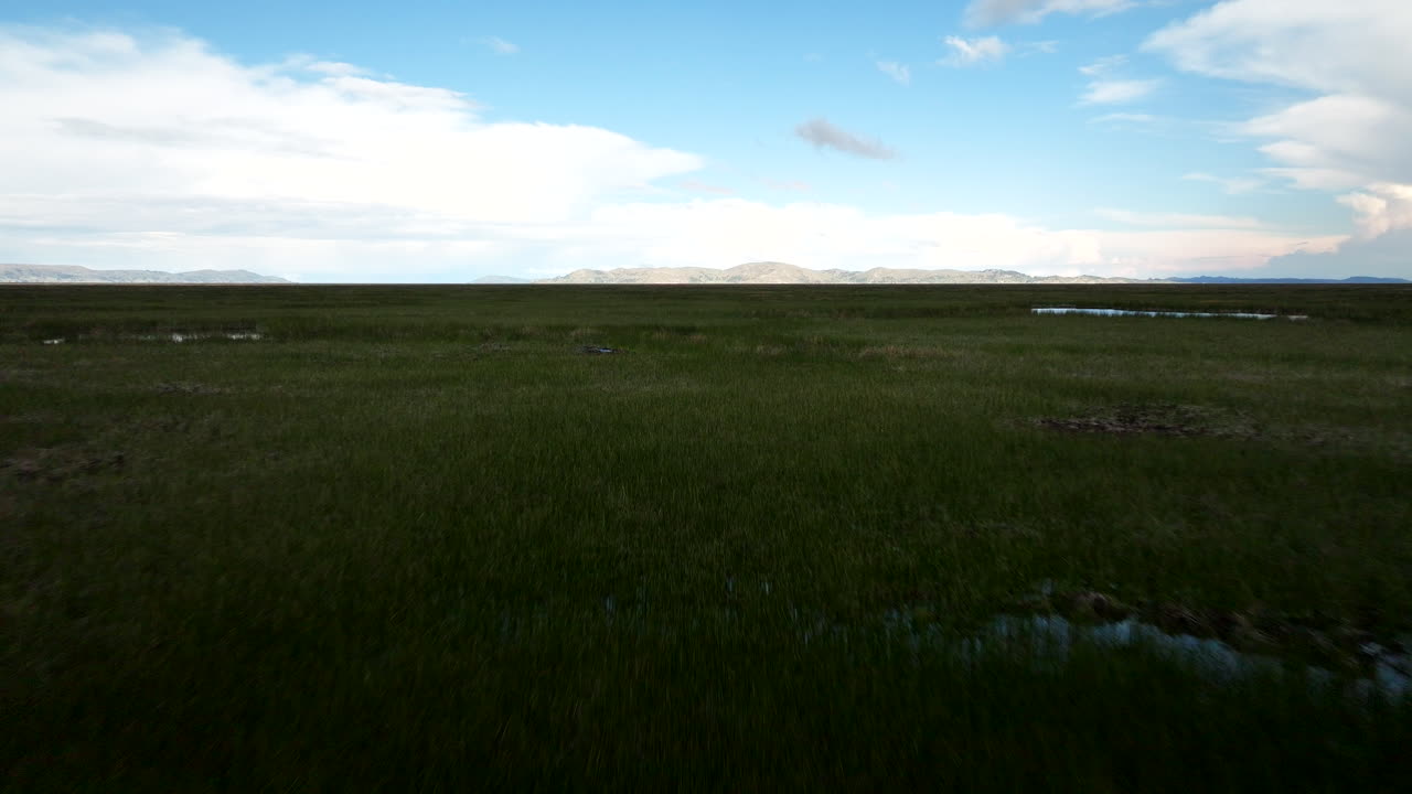 Bredt luftperspektiv af Lake Titicacas vådområder nær Uros-øerne med vidtstrakt åbent vand og glimt af blå refleksioner i det høje græs
