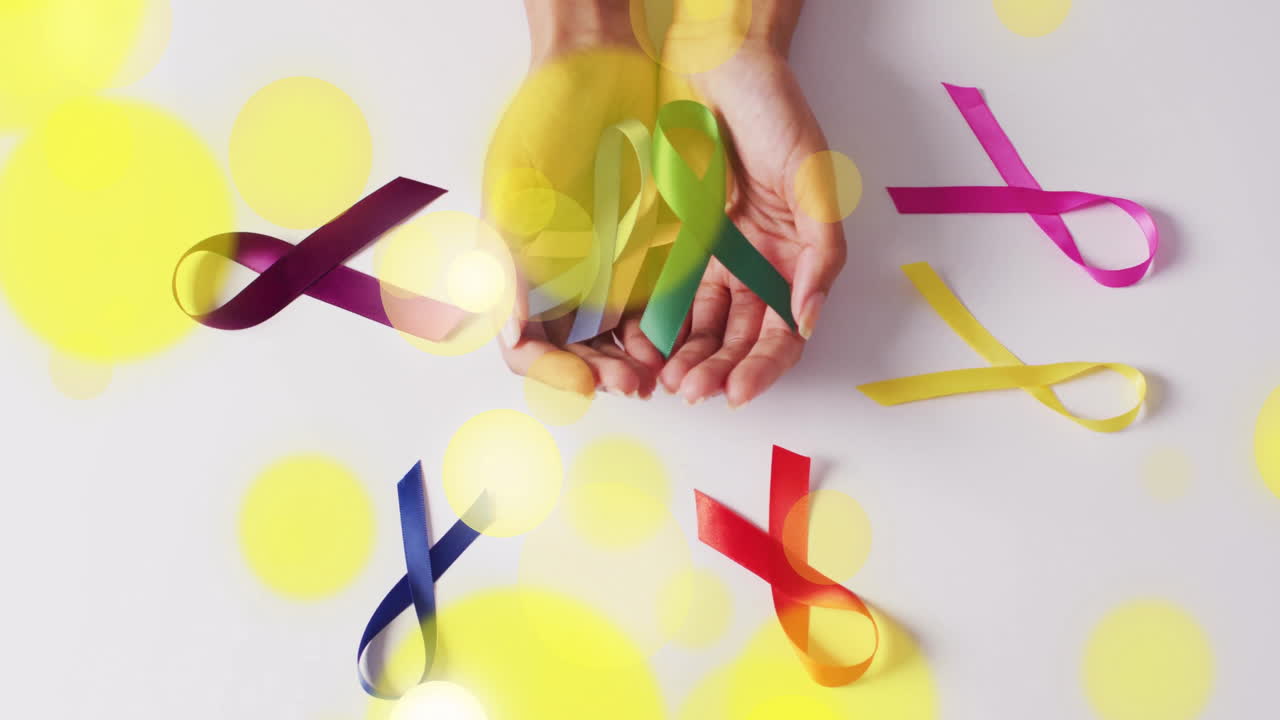 Holding colorful awareness ribbons, hands with bright yellow light spots overlay