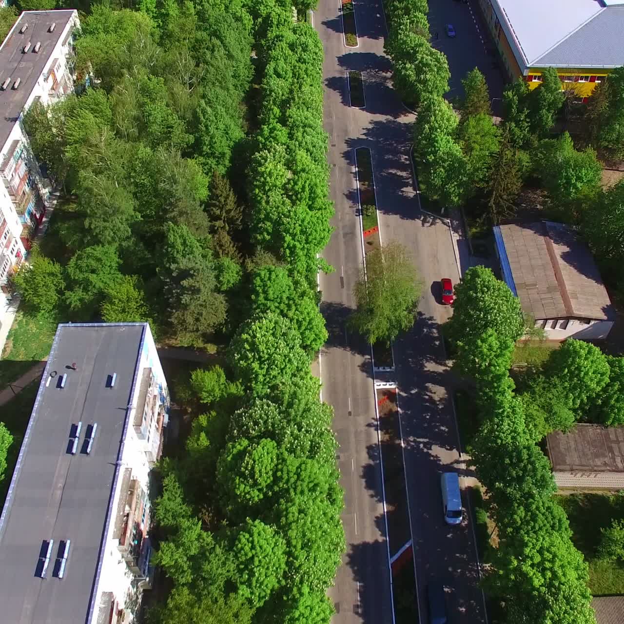 Two-ways road passing through the city. Drone flying along the way to the outlook of a beautiful sunny city at the backdrop of nature