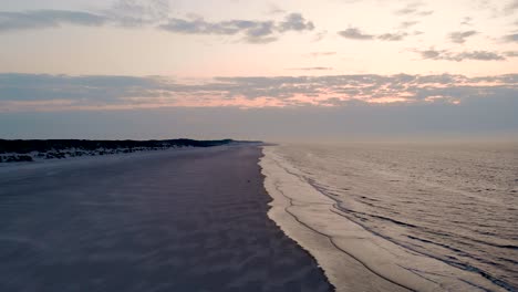 drone over calm waves at beach with pink hue from sunset sky in langeoog island, germany