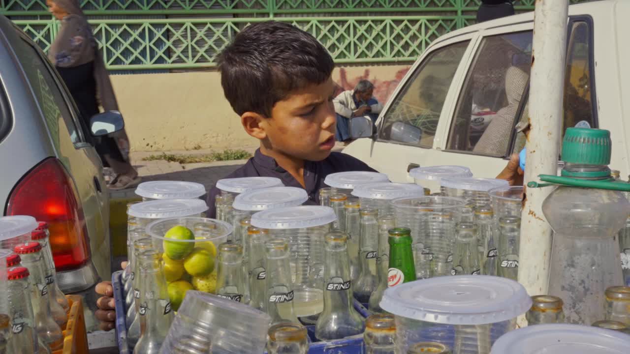Young street vendor enthusiastically offers homemade lemon soda to thirsty customers from a colorful cart in a lively marketplace.