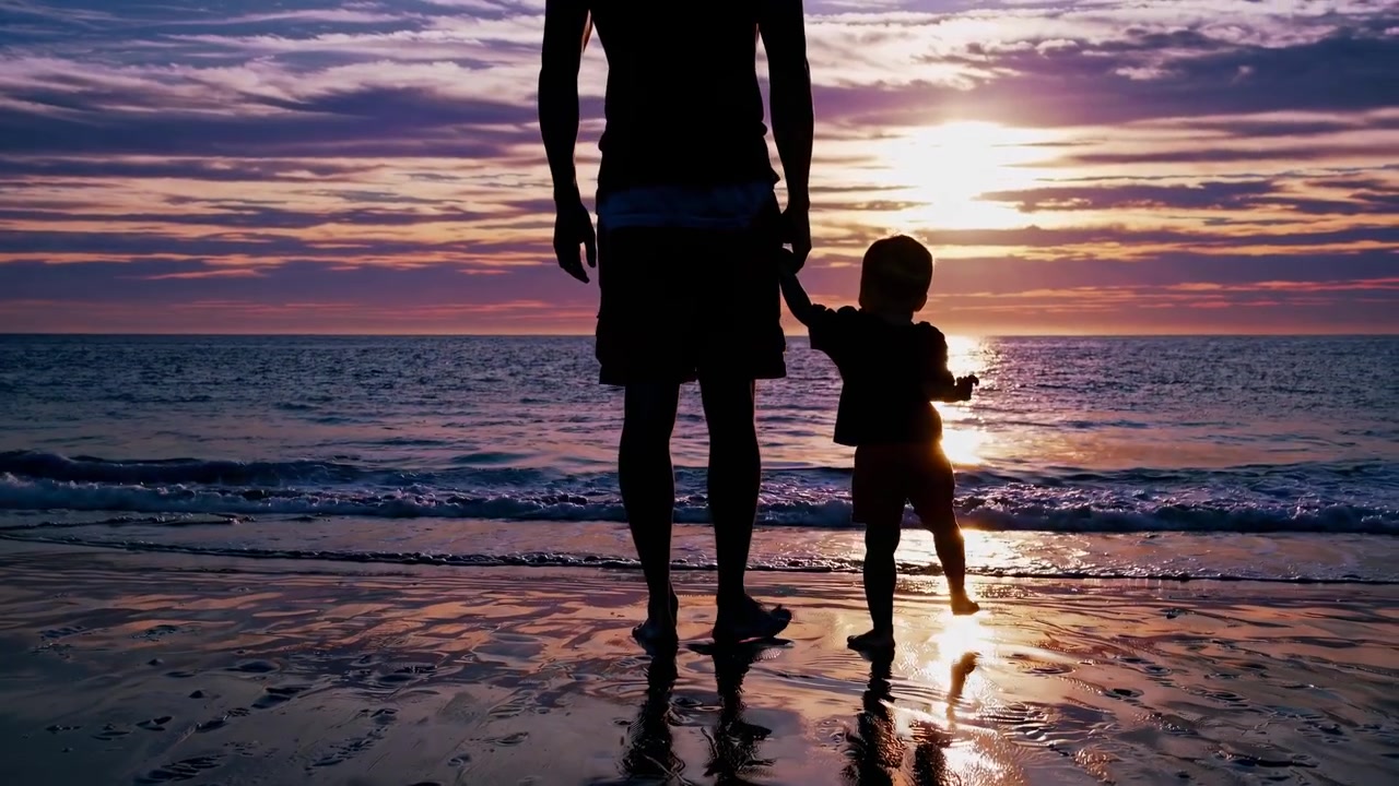 Silhuet af far og søn, der holder i hånd på stranden ved solnedgang