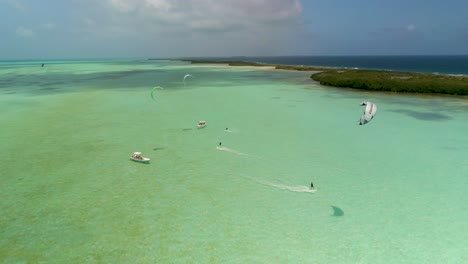 Giro-Aéreo-Alrededor-De-Los-Kitesurfistas-Se-Deslizan-Sobre-Aguas-Planas,-Manglares-Y-Botes-En-Salinas,-Los-Roques