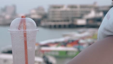 straw in plastic cup with water against large hotel resort