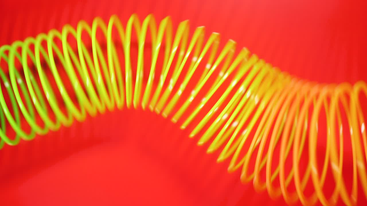 Vintage Retro Abstract Background. Rainbow Coloured Spring Moves Across a Red Background In a Wave Like Pattern. Slinky Toy. Rainbow Spiral Spring Motion Wave a Bright Beautiful Background.