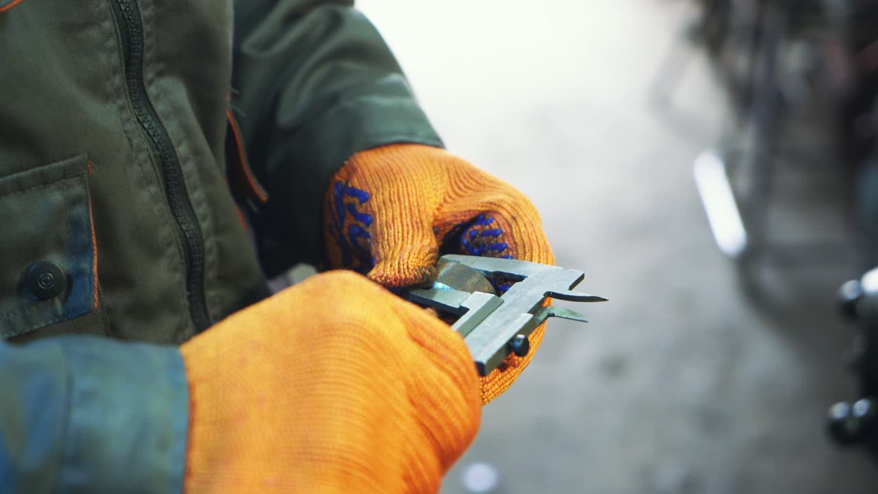 Industrial worker is working on metal work factory process by performing mechanical turning operation at machine for steel structure industry. Hands close up.