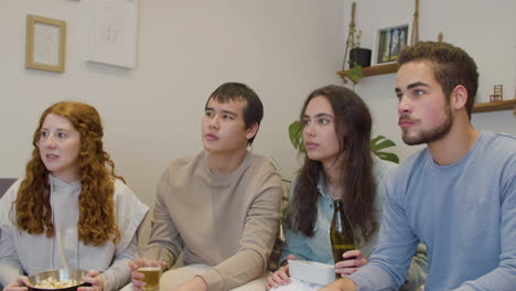 focused friends sitting on sofa and watching sports game on tv