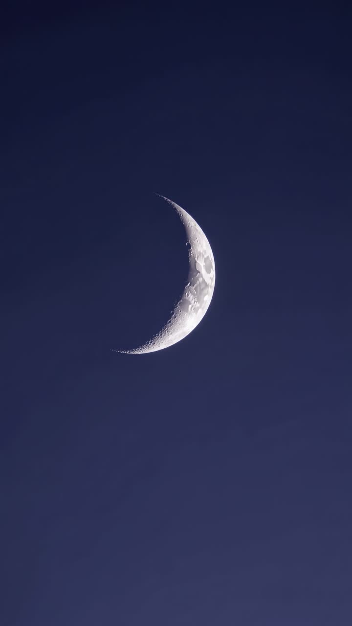 Uma lua crescente contra um céu azul profundo, capturada em close-up, em um ângulo ascendente.