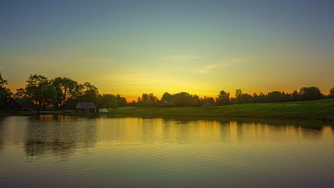 Zeitraffer-Eines-Sees-Bei-Sonnenuntergang-Mit-Blauem-Und-Gelbem-Himmel-Und-Wolken,-Die-Sich-Im-Wasser-Spiegeln