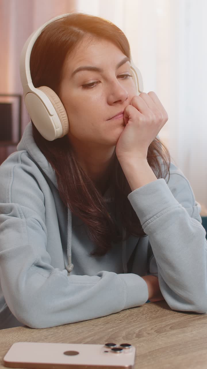 Young caucasian woman listening to audiobook on smartphone with wireless headphones sitting on sofa