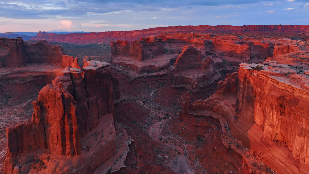Il sole al tramonto illumina le ripide pareti di roccia rossa. Filmato aereo lungo i canyon nell'Arches National Park, USA