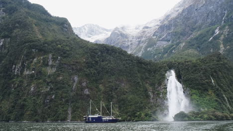Segelboot-Vor-Einem-Riesigen-Wasserfall,-Umgeben-Von-üppig-Grünen-Klippen-Und-Glitzerndem-Blauem-Wasser