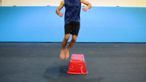 a still shot of a guy in a gymnastics gym doing jumps from side to side from a front view