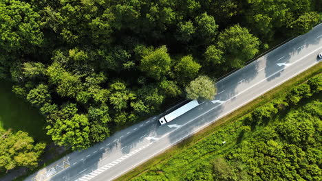 following a white big lorry moving by the highway in the countryside. lush green woods around the road. top view.