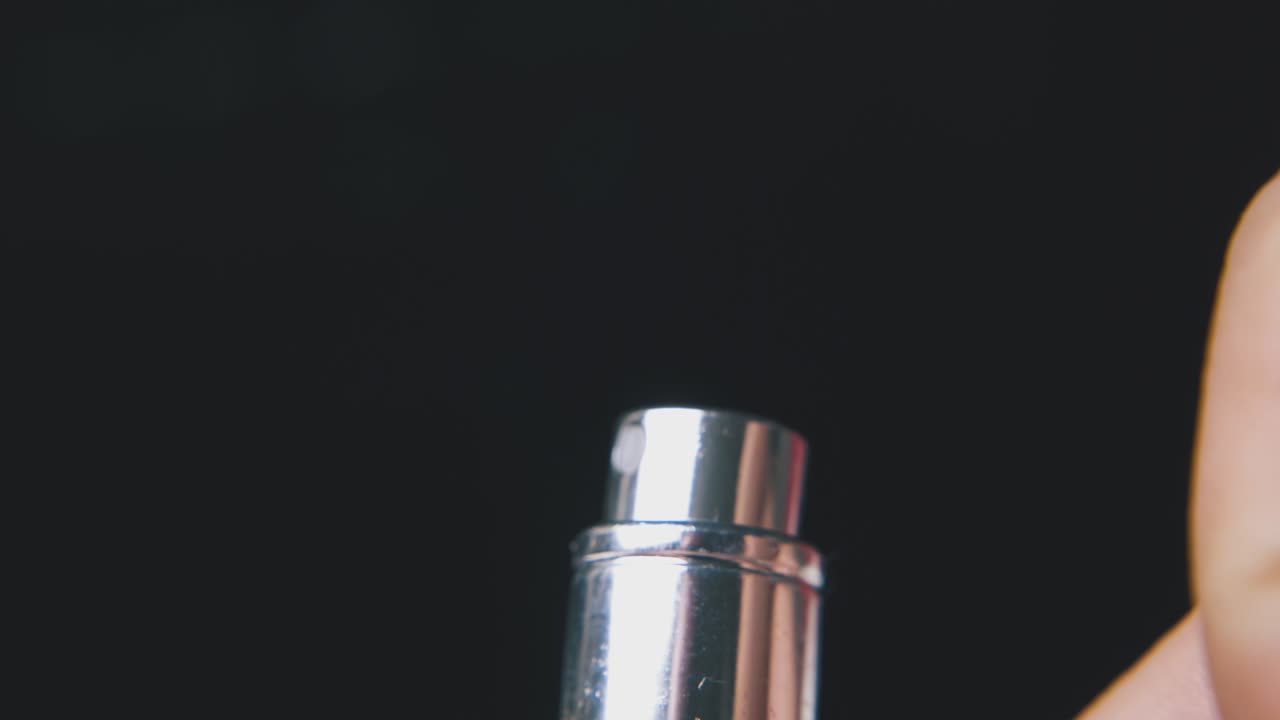 man sprays and closes perfume in bottle on dark background