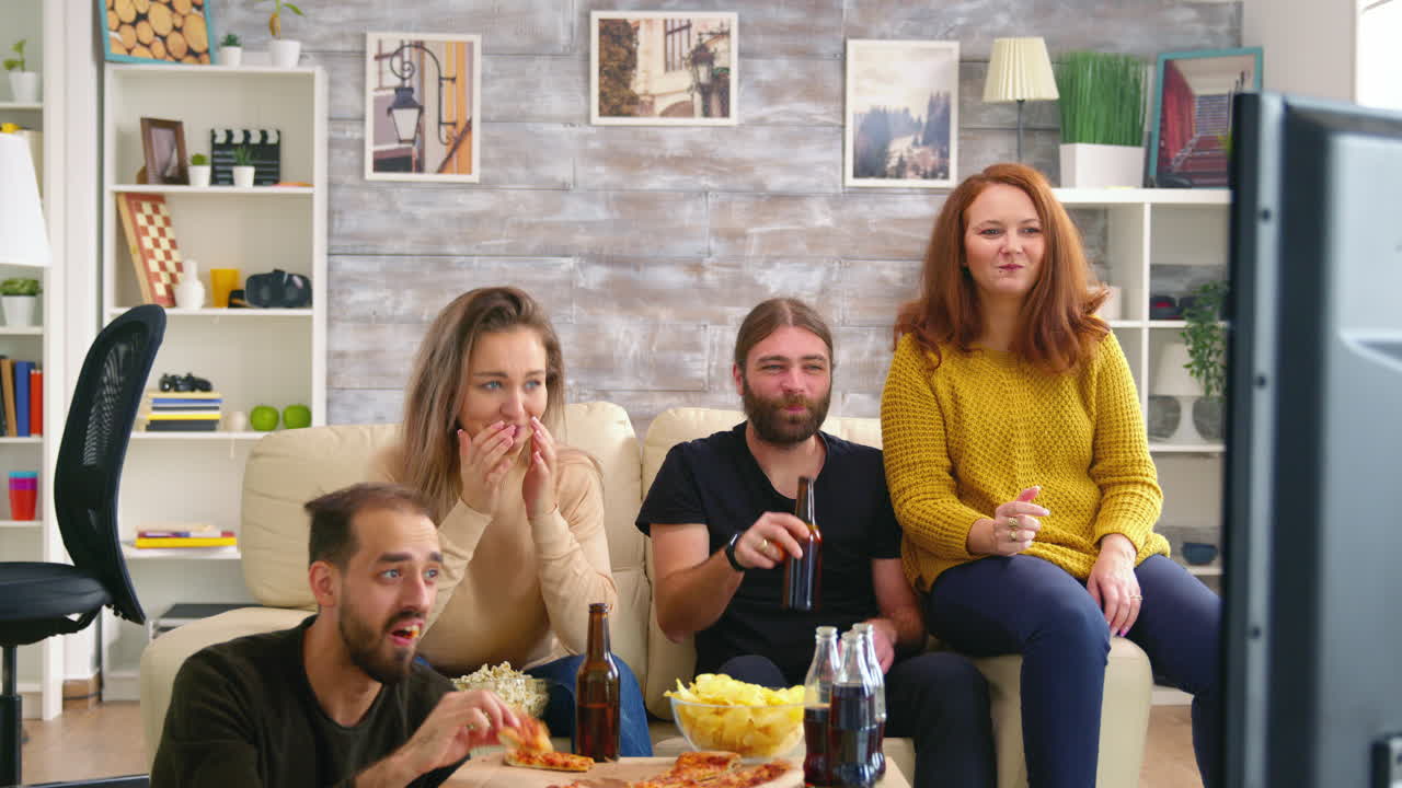 Giovane uomo che applaude mentre guarda un film in TV con i suoi amici.