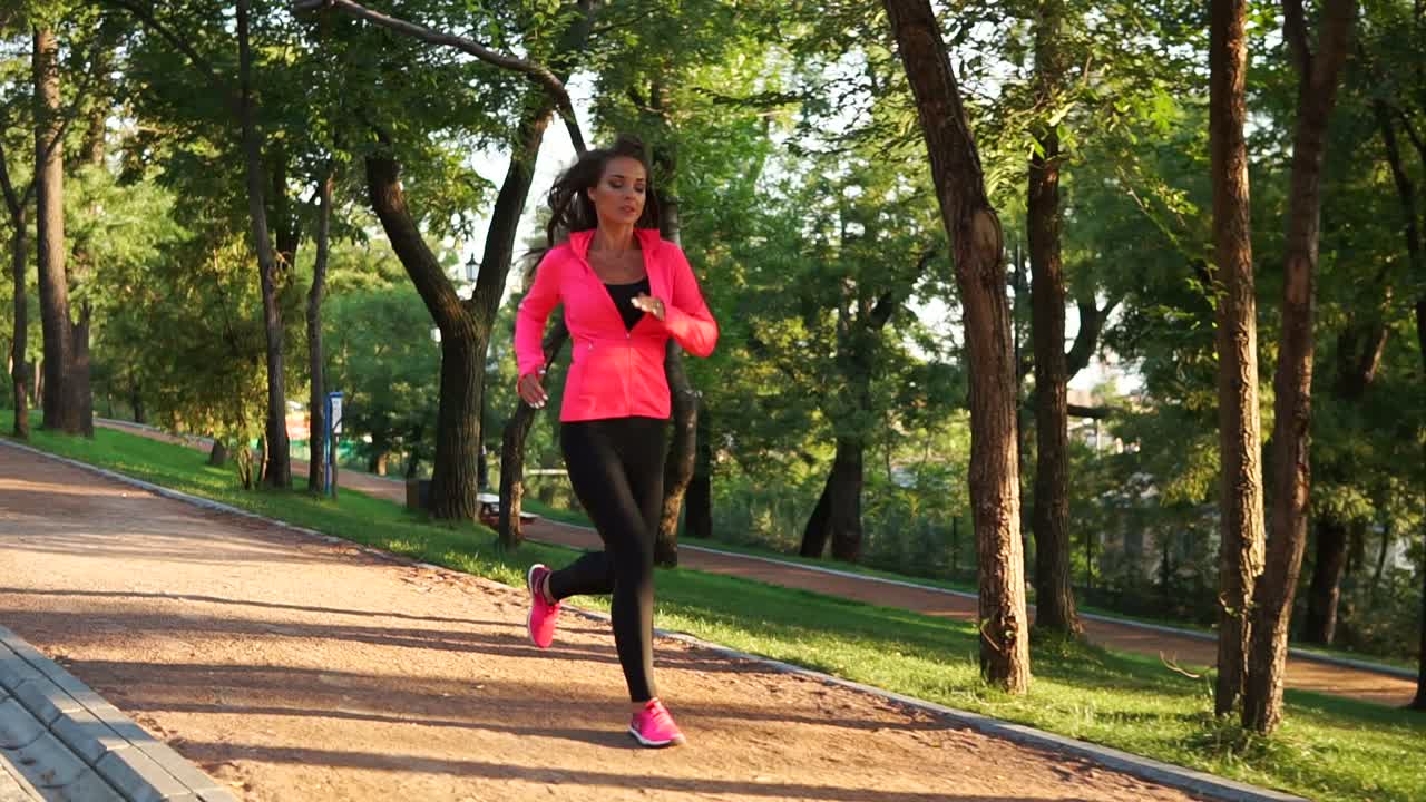 mujer joven corriendo en el parque de la ciudad soleada haciendo ejercicio al aire libre. steadicam estabilizado disparo, cámara lenta. ejercicio matutino