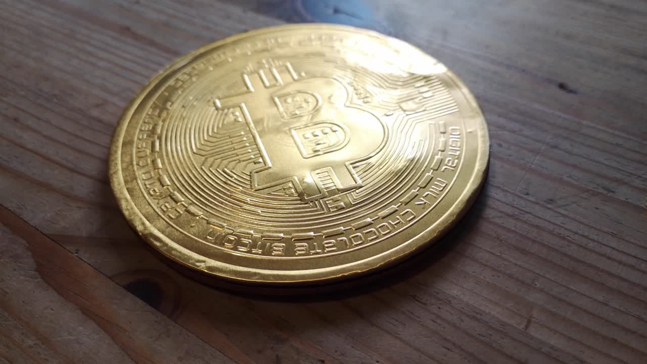 concepto de moneda criptográfica de bitcoin de oro chocolate envuelto en la mesa de la cocina de madera órbita izquierda mirando hacia abajo