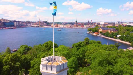 aerial view capturing kastellet in stockholm with a swedish flag waving, surrounded by lush greenery and overlooking the scenic waterfront and cityscape