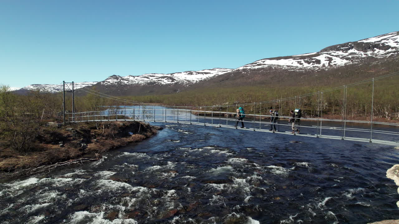 Three Hikers Walking over a Suspension Bridge on the Kungsleden near Abiskojaure in The Swedish Mountains, Backpacking in the Forest, Wide Shot