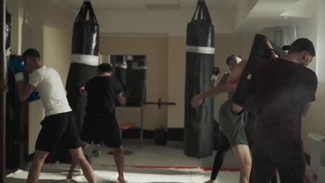 los boxeadores robustos ejecutan la técnica de golpeo adecuada utilizando equipos especializados y bolsas de boxeo. sesión de entrenamiento en grupo en un club deportivo. orientación del instructor a los participantes