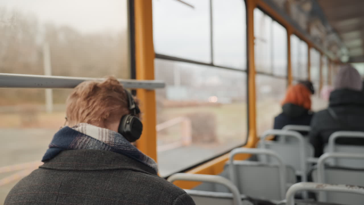 Adolescente con le cuffie esamina l'ambiente suburbano che scorre dal sedile dell'autobus. Giovane uomo con le cuffie riflette in silenzio sulla vista suburbana fuori dal finestrino dell'autobus durante un viaggio tranquillo.