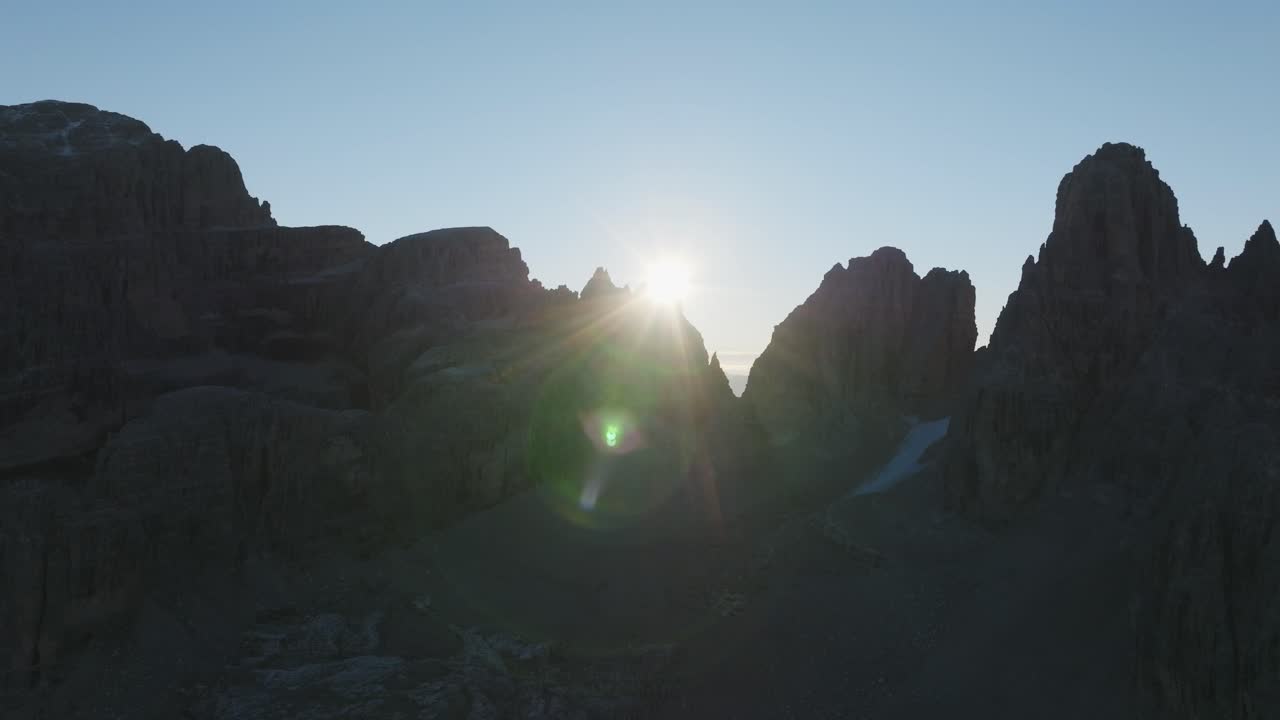 vista aérea del sol escondiéndose detrás de los picos de las montañas durante la puesta de sol en dolomitas - toma amplia