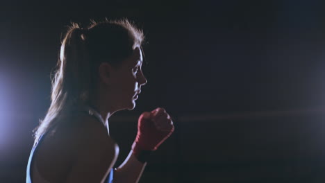 A-beautiful-sports-boxer-woman-in-red-bandages-on-her-hands-and-a-blue-t-shirt-is-fighting-with-a-shadow-practicing-the-speed-and-technique-of-punches.-Camera-movement-side-View.-Steadicam-shot.-Preparing-for-self-defense