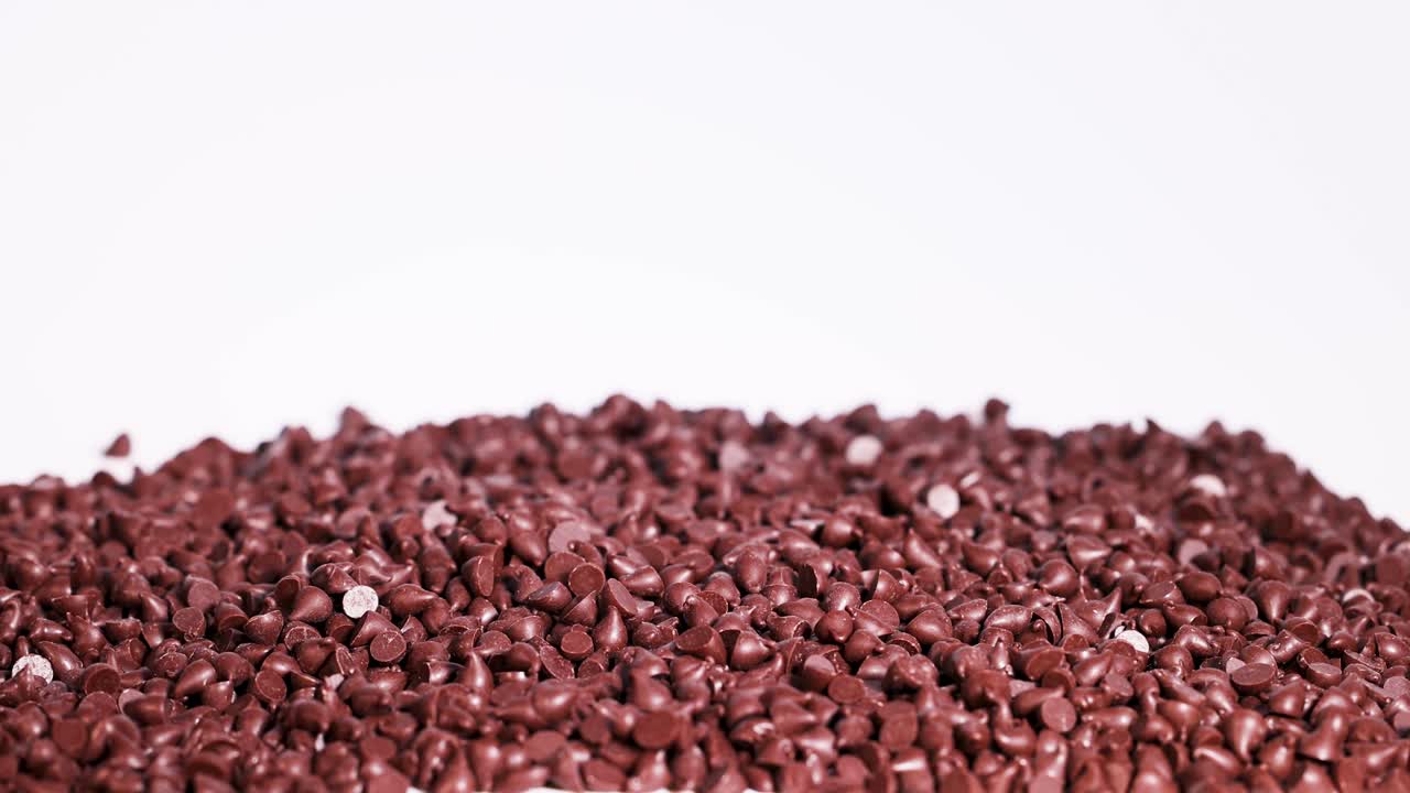 Chocolate drops cascade onto a pile against a white background, captured in slow motion with consistent lighting