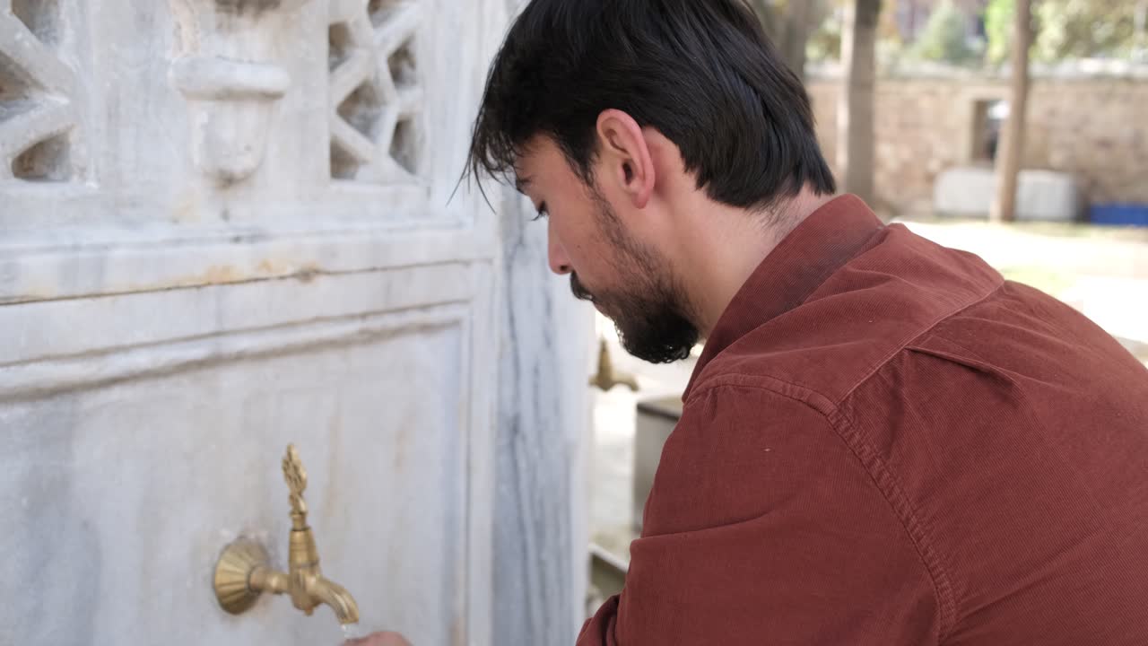 Back view of Muslim bearded man performing ablution, man washing his hair at mosque fountain, bearded youth performs ablution before prayer