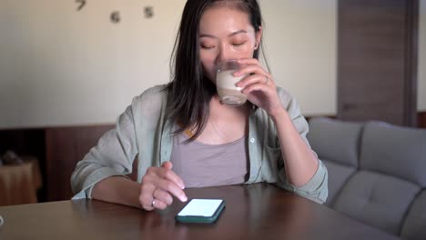 Asiatische-Frau-Mit-Latte,-Die-Den-Bildschirm-Auf-Dem-Smartphone-Berührt