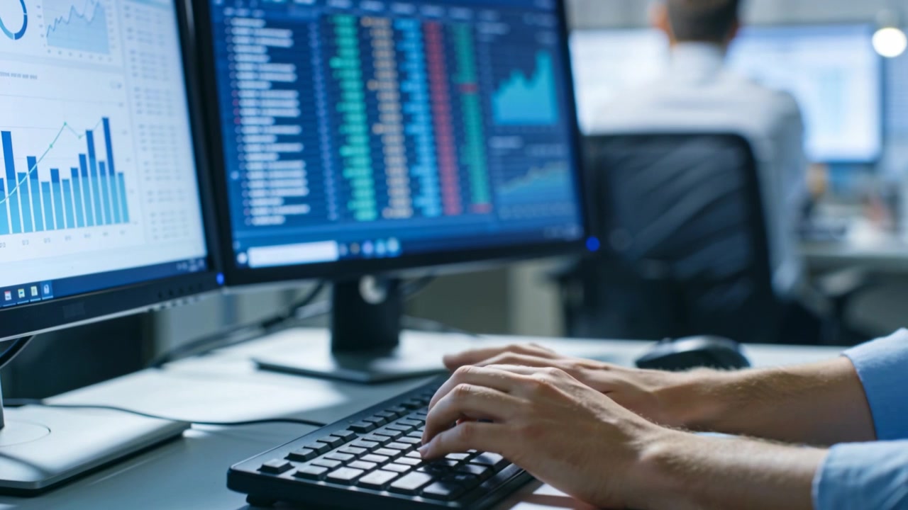 Reacting to chart updates analyst hands blue shirt tapping keys at desk monitoring two screens