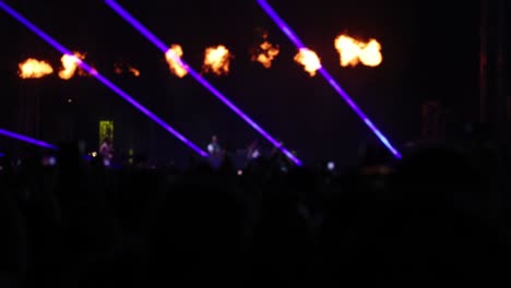 Concert-stage-illuminated-by-neon-flashing-lights-and-flames,-band-playing-music